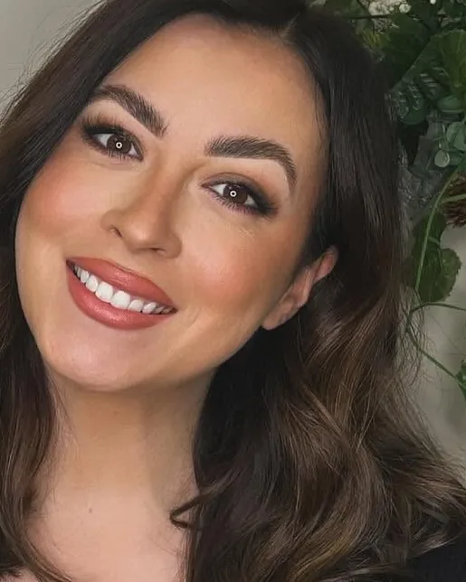 Alanna Starr, makeup artist, smiling in close-up wearing a soft smoky eye and warm nude lip.
