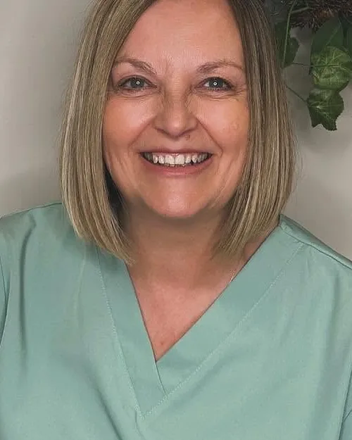 Michelle Starr, aesthetician and registered nurse, in sage green scrubs, smiling in the studio treatment area.