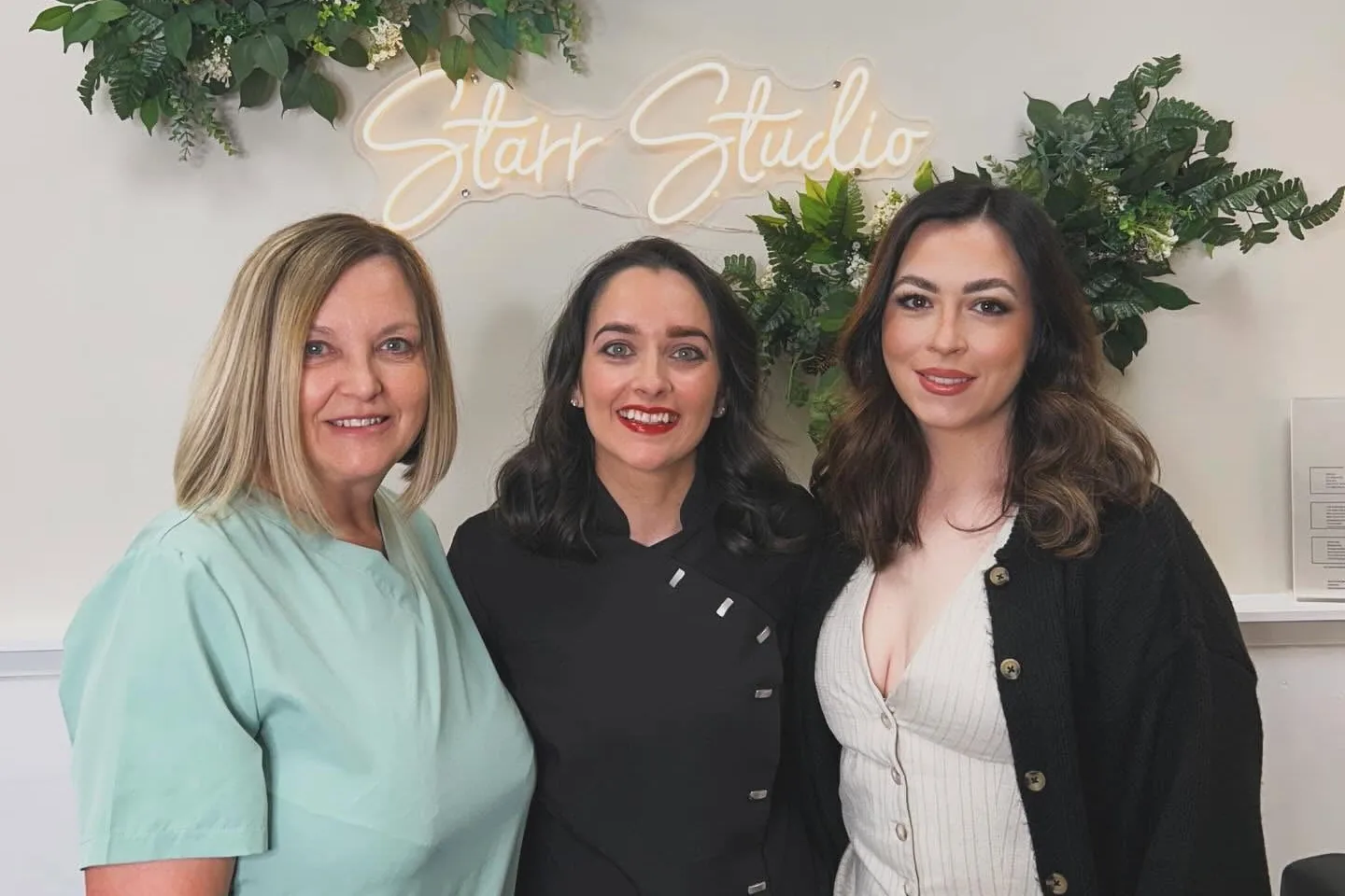 Michelle, Rachel and Alanna Starr together in the studio, standing under the lit Starr Studio neon sign surrounded by greenery.